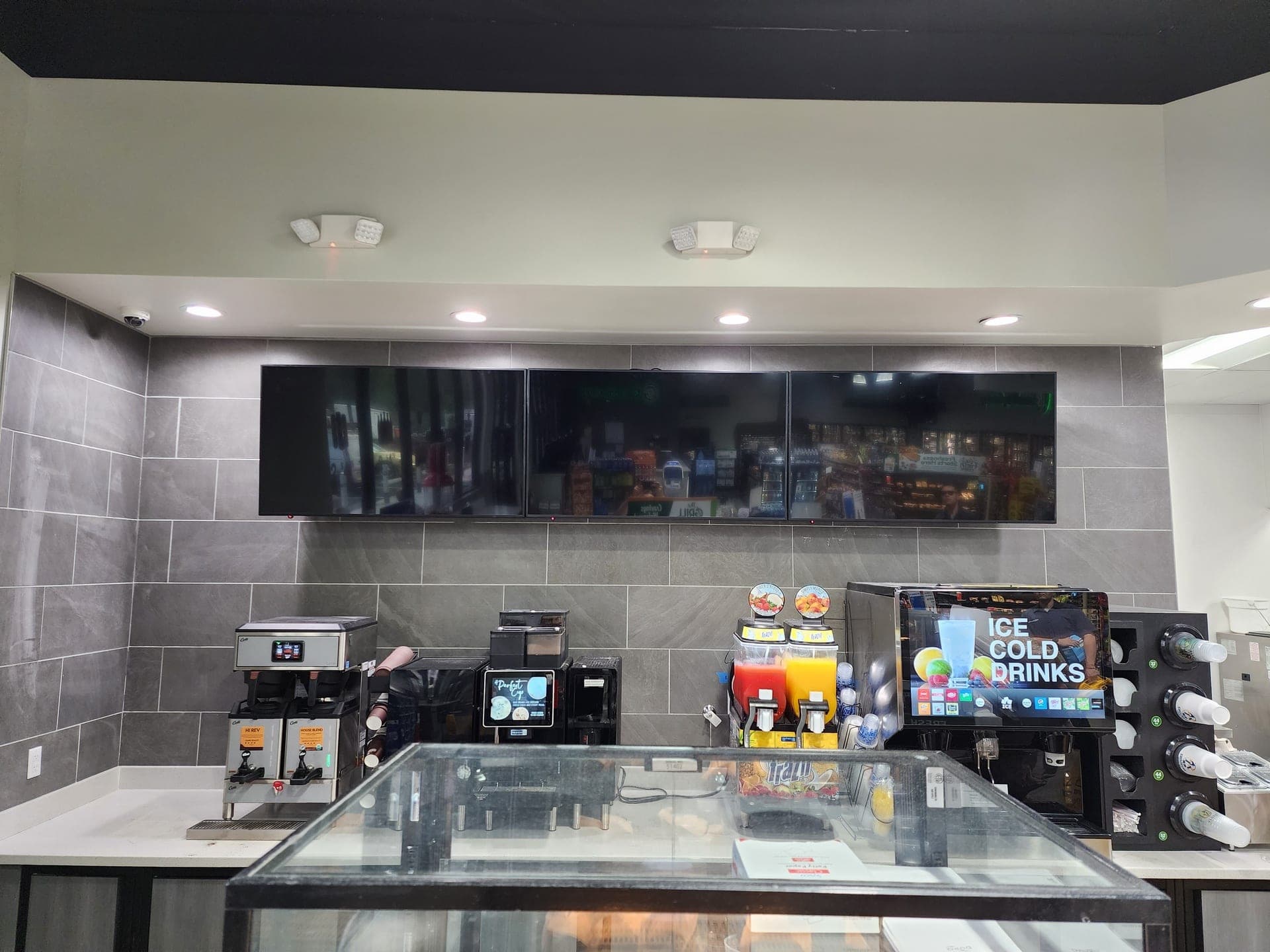 Three-screen digital menu board above a coffee counter