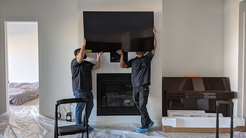 Two technicians mounting a TV above a fireplace